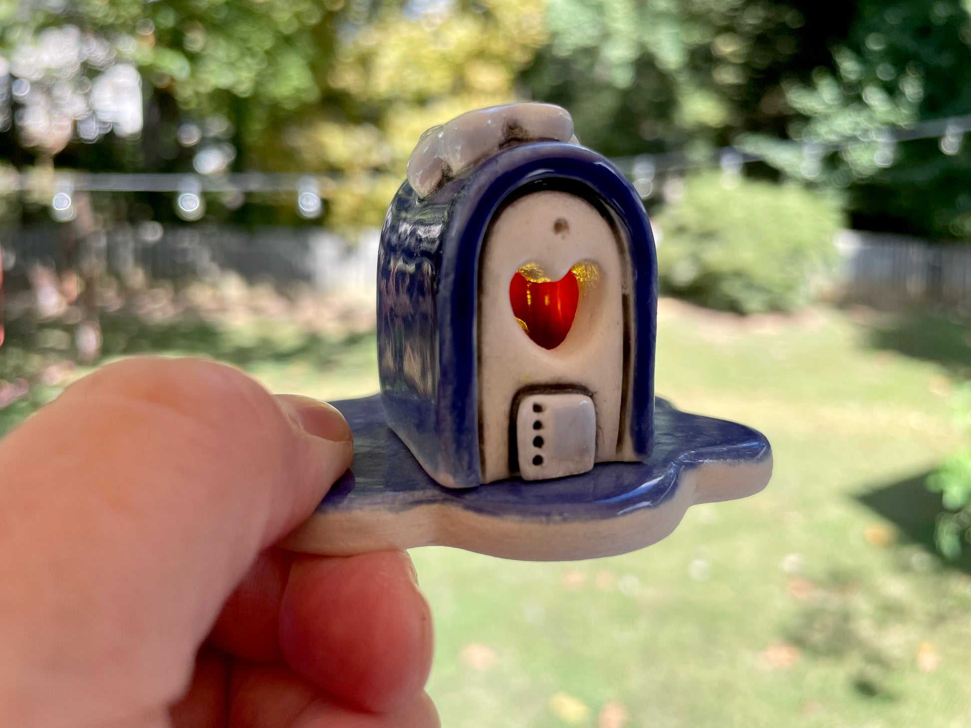 Small ceramic house with a red heart on a blurred outdoor background