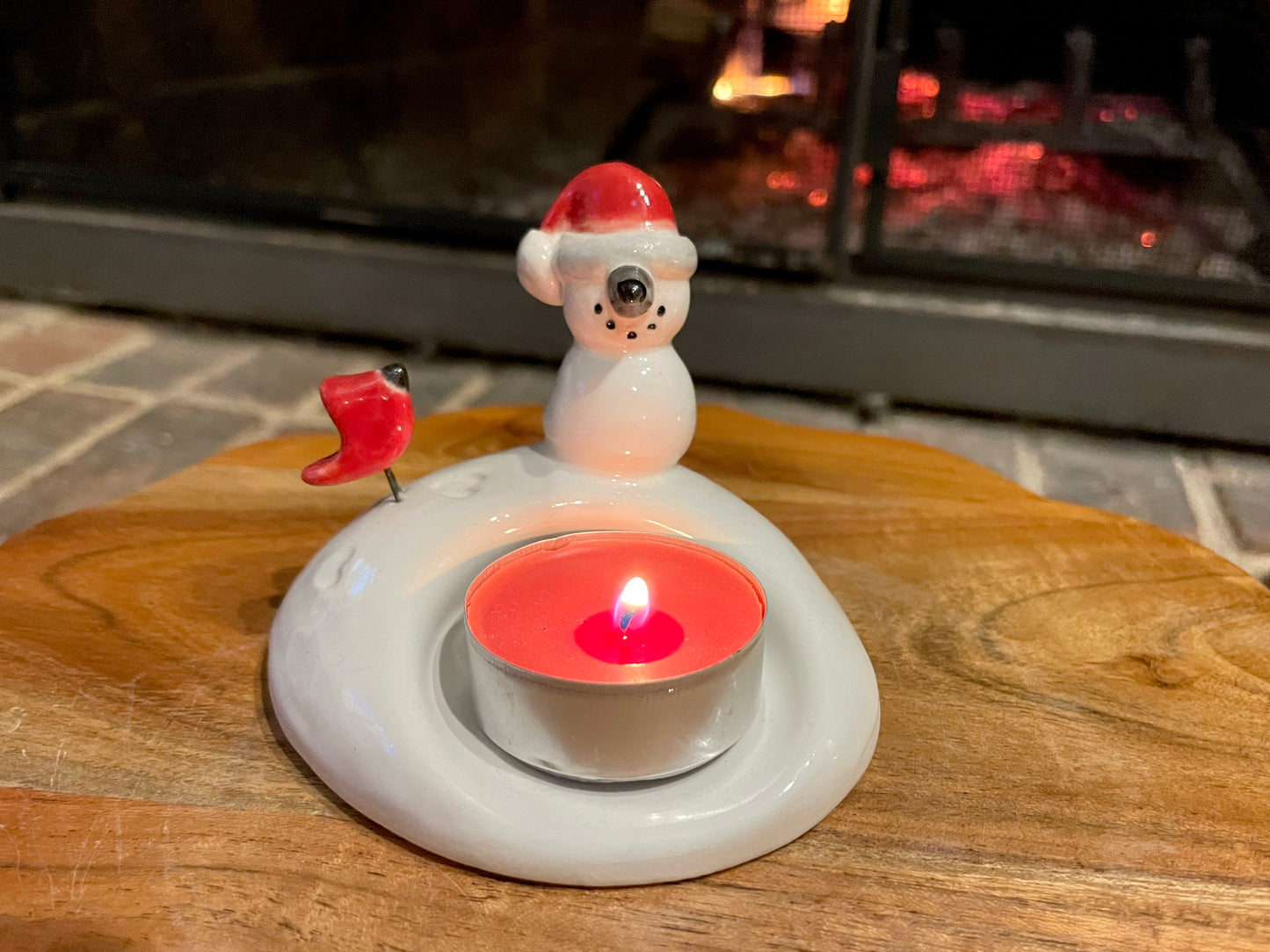 Ceramic snowman candle holder with a lit candle. Close-up of white, red, and black glazed snowman candle holder.