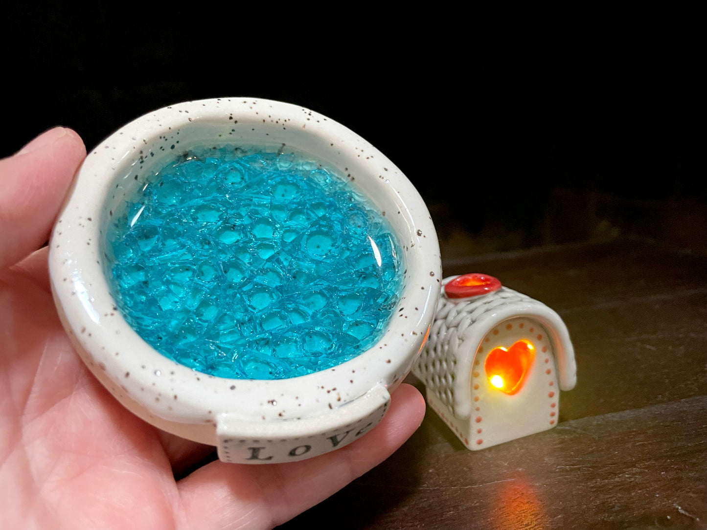 Handmade ceramic Christmas cabin glowing with LED light beside a frozen lake incense burner.