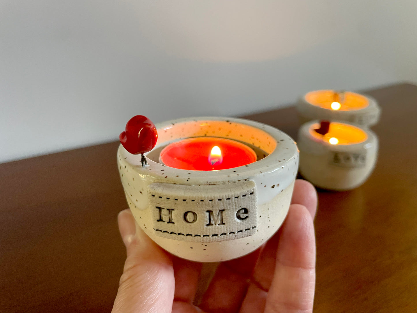 Ceramic candle holder with 'HOME' text, lit candle inside. Handmade ceramic frozen lake candle holder with tiny red cardinal, white glaze, and smooth clay finish.