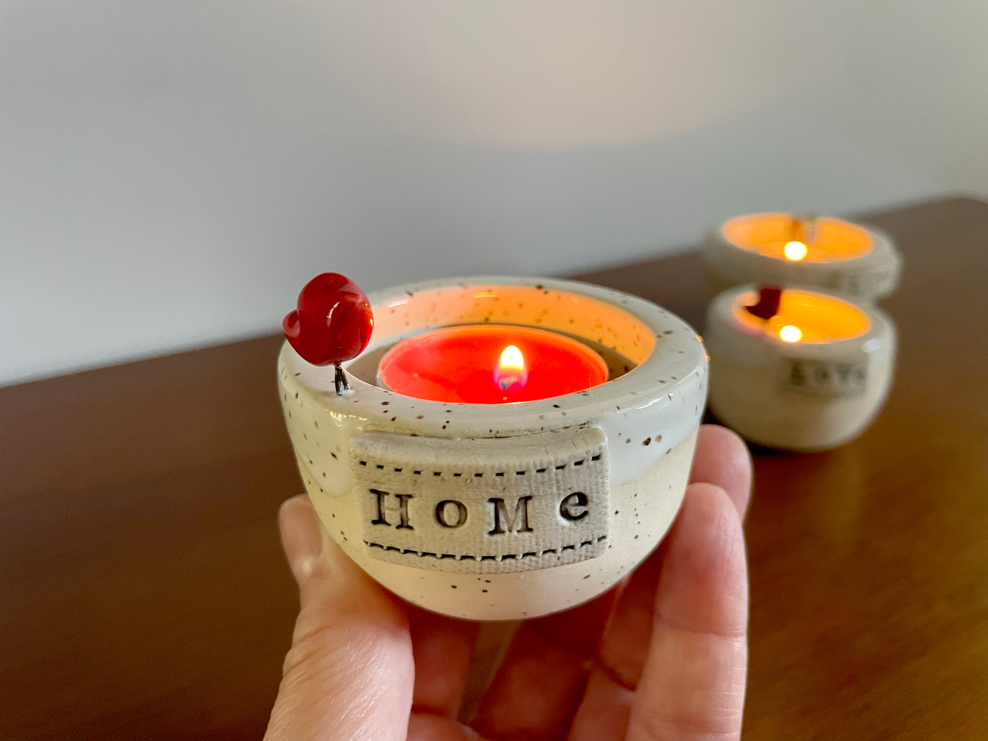 Ceramic candle holder with 'HOME' text, lit candle inside. Handmade ceramic frozen lake candle holder with tiny red cardinal, white glaze, and smooth clay finish.