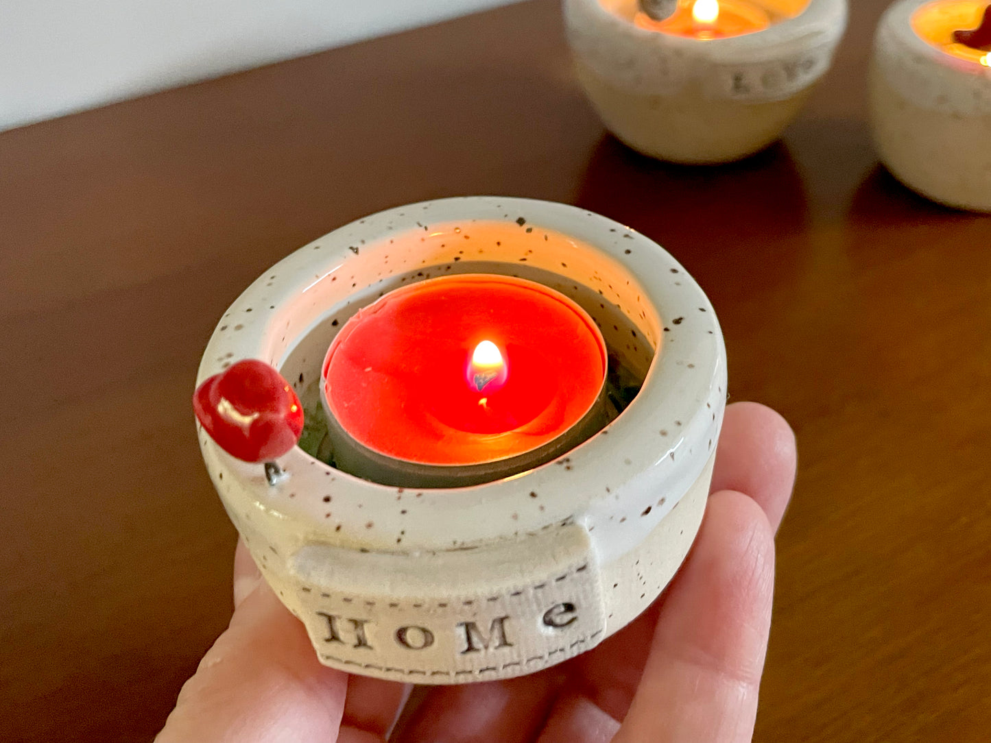 Close-up of tiny red cardinal bird on white glazed frozen lake ceramic dish for tea light candle. Small ceramic candle holder with a lit candle, labeled 'Home'.