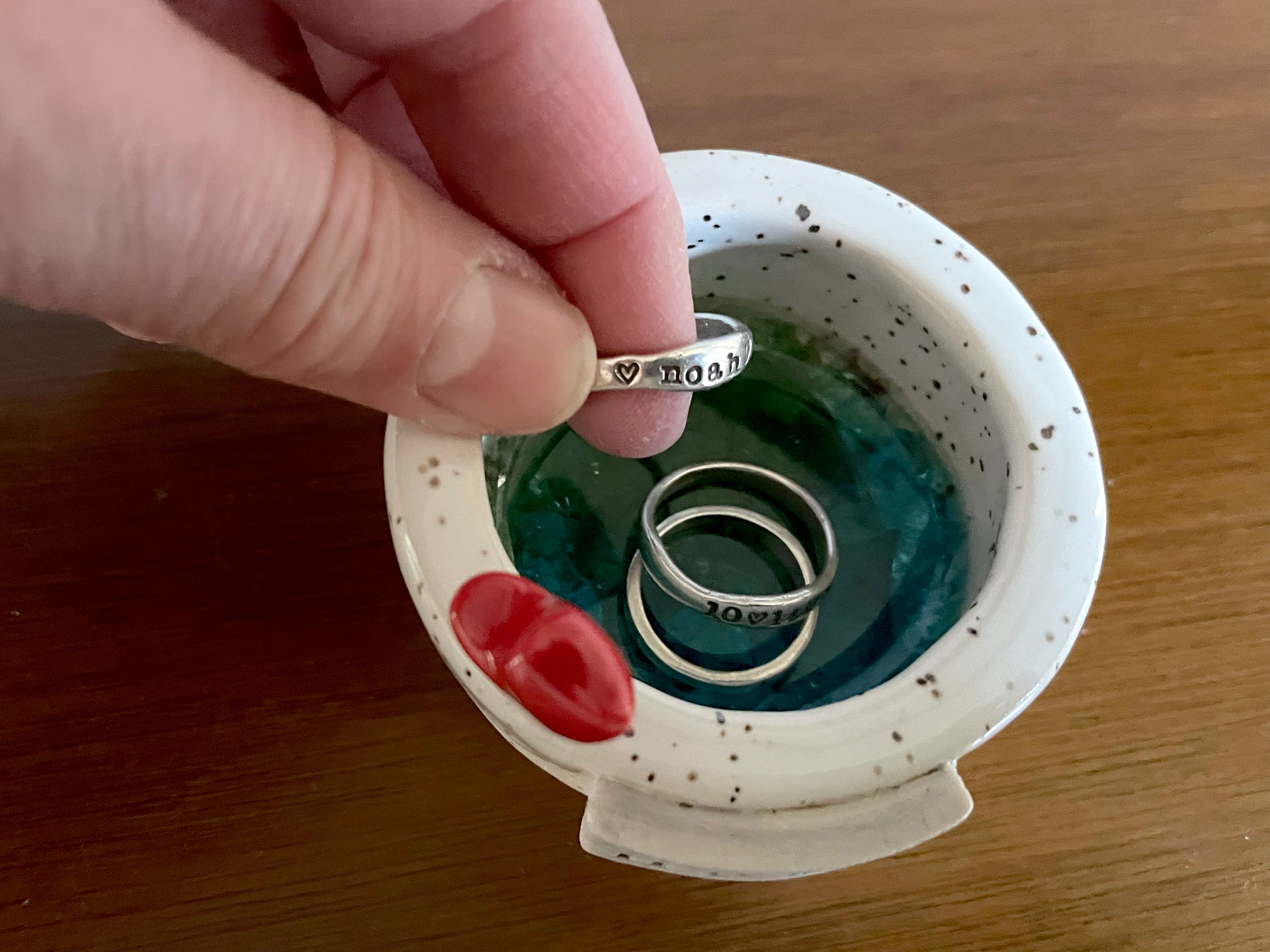 Cozy holiday scene with handmade ceramic candle holder glowing on table — winter home décor piece. Hand holding a silver ring above a small ceramic dish with two other rings inside.