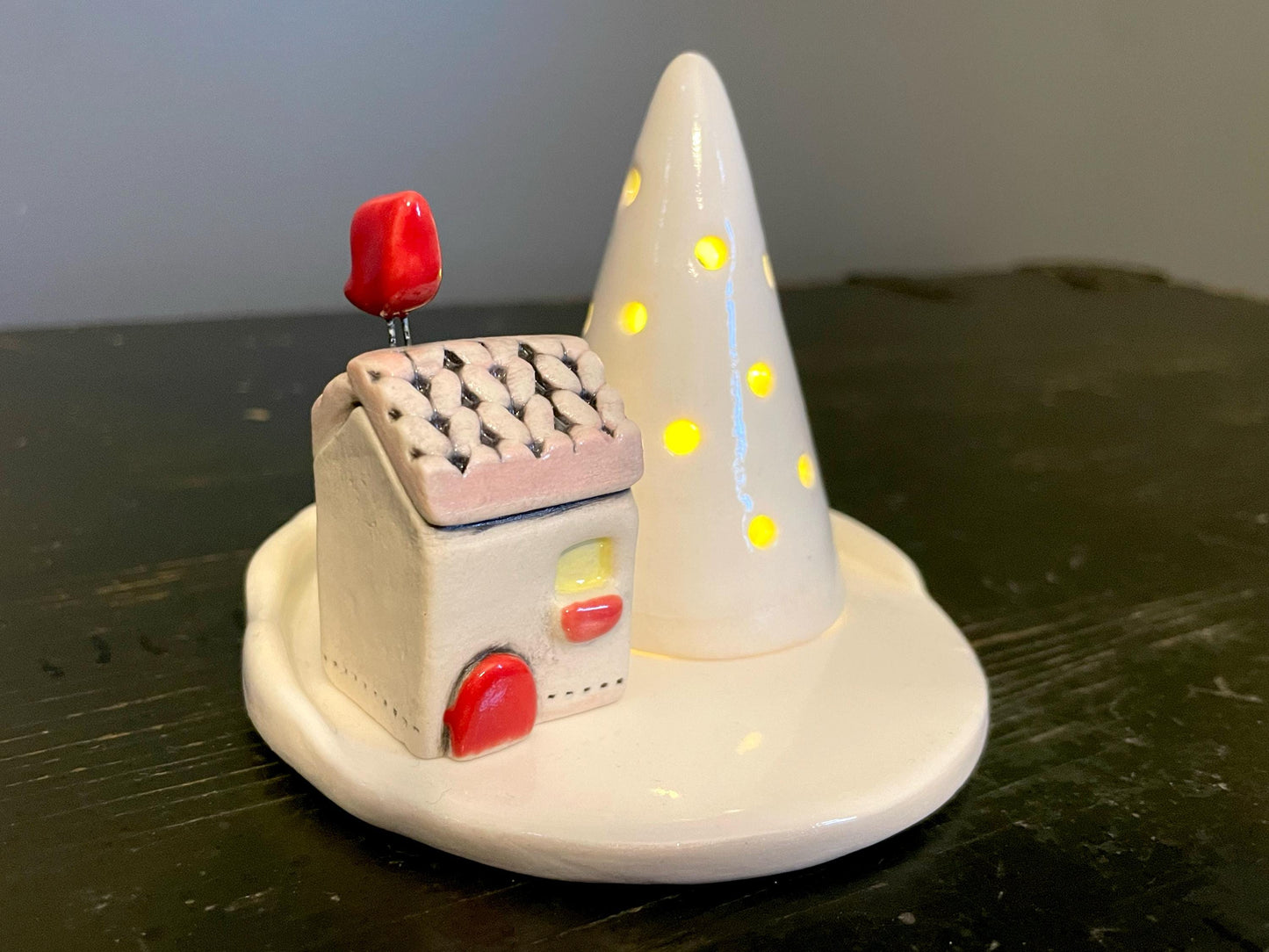 Decorative house and tree figurine on a dark surface with a plain background