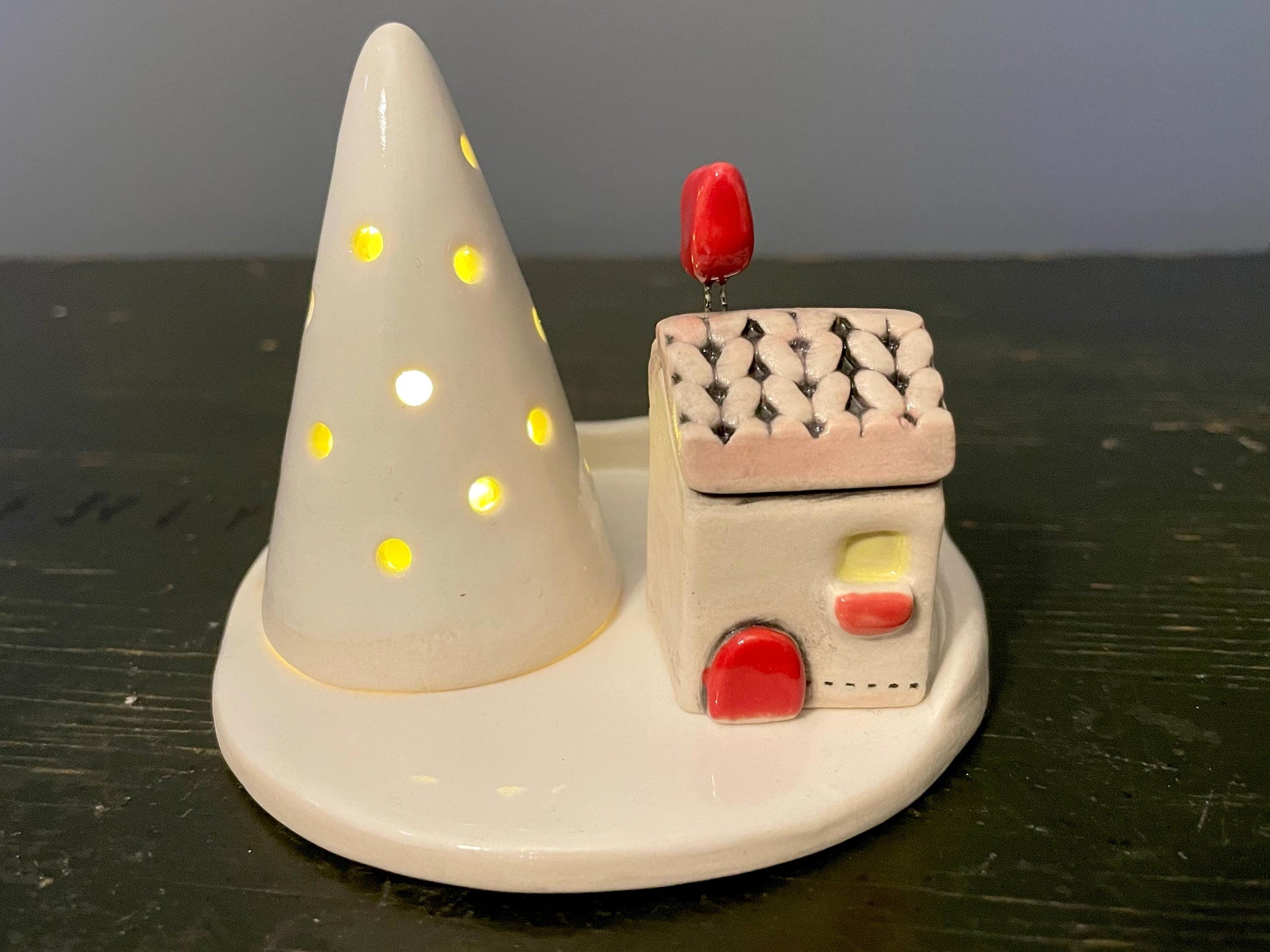Ceramic house with a red roof and cone-shaped light on a dark surface