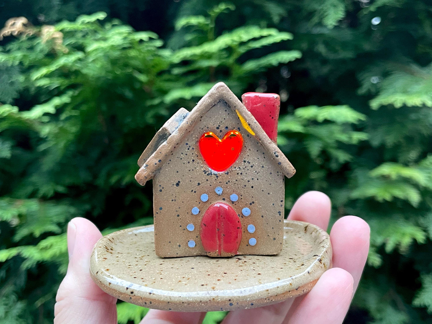 Small ceramic house with a red heart on a green blurred background