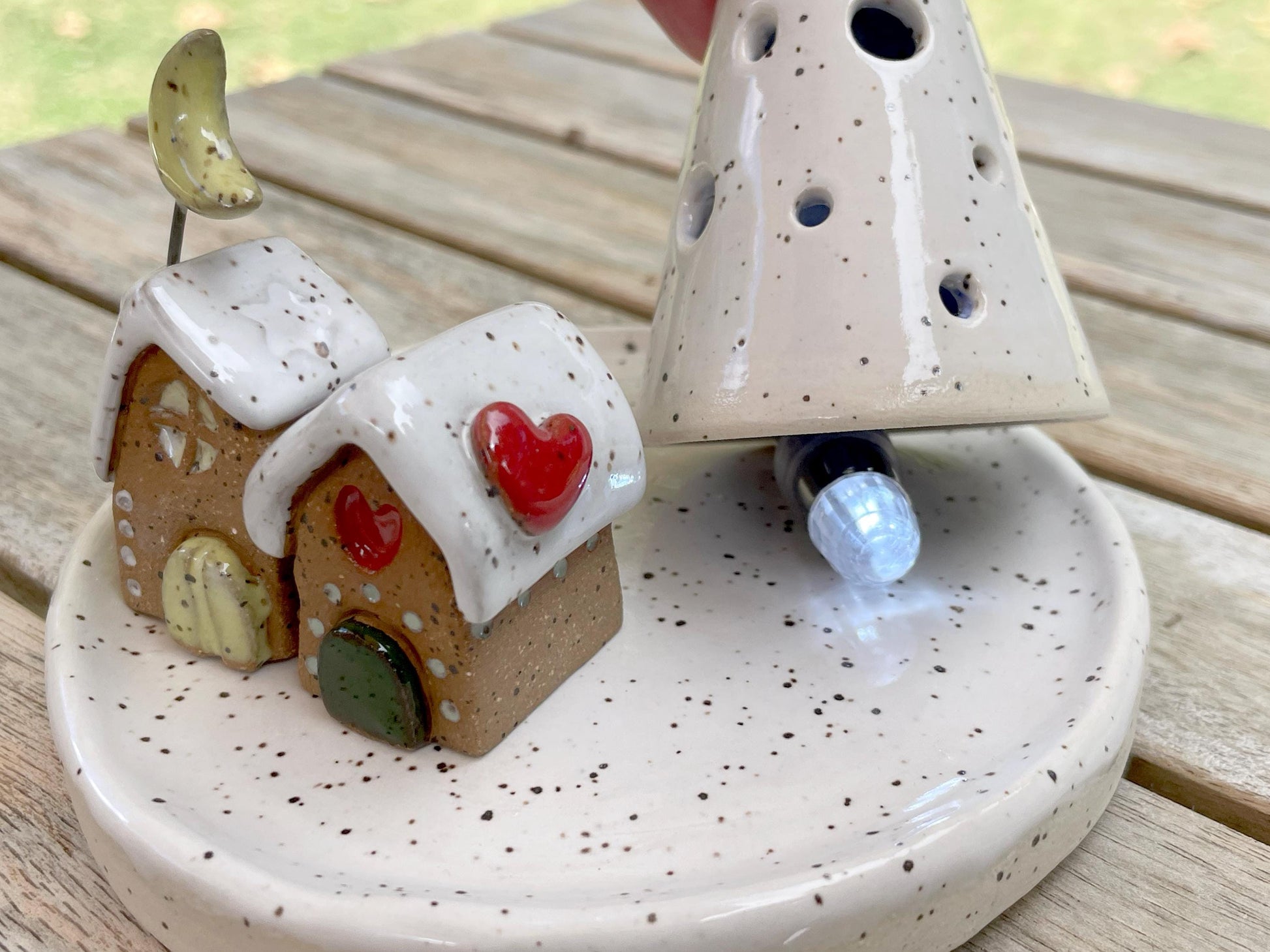 Ceramic gingerbread house with a heart on a speckled ceramic base.