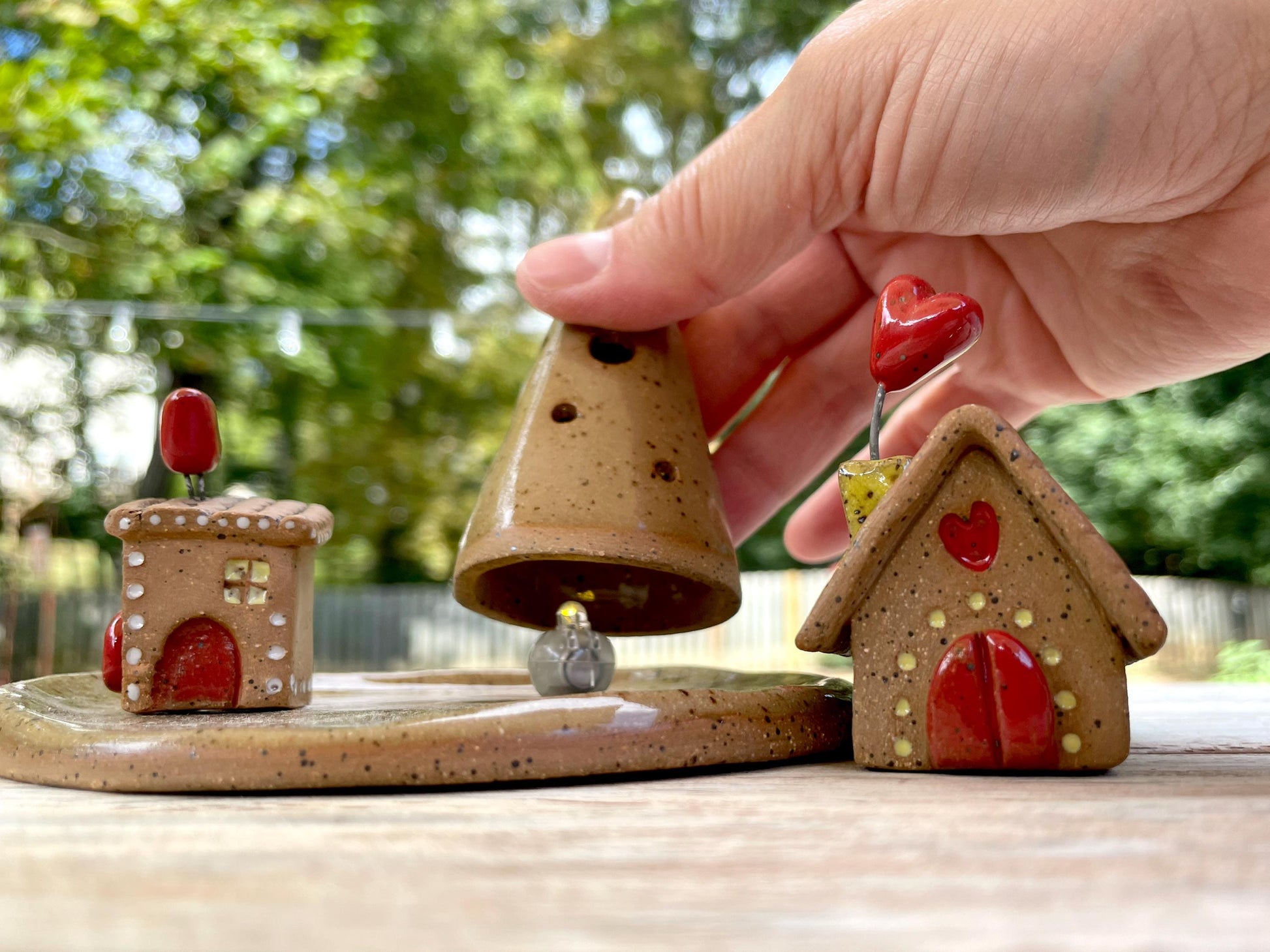 Ceramic bell with two small houses on a wooden surface outdoors