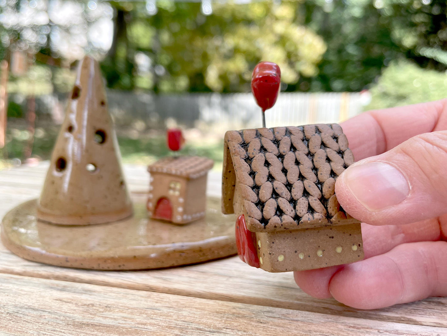 Hand holding a small ceramic house model with a blurred outdoor background