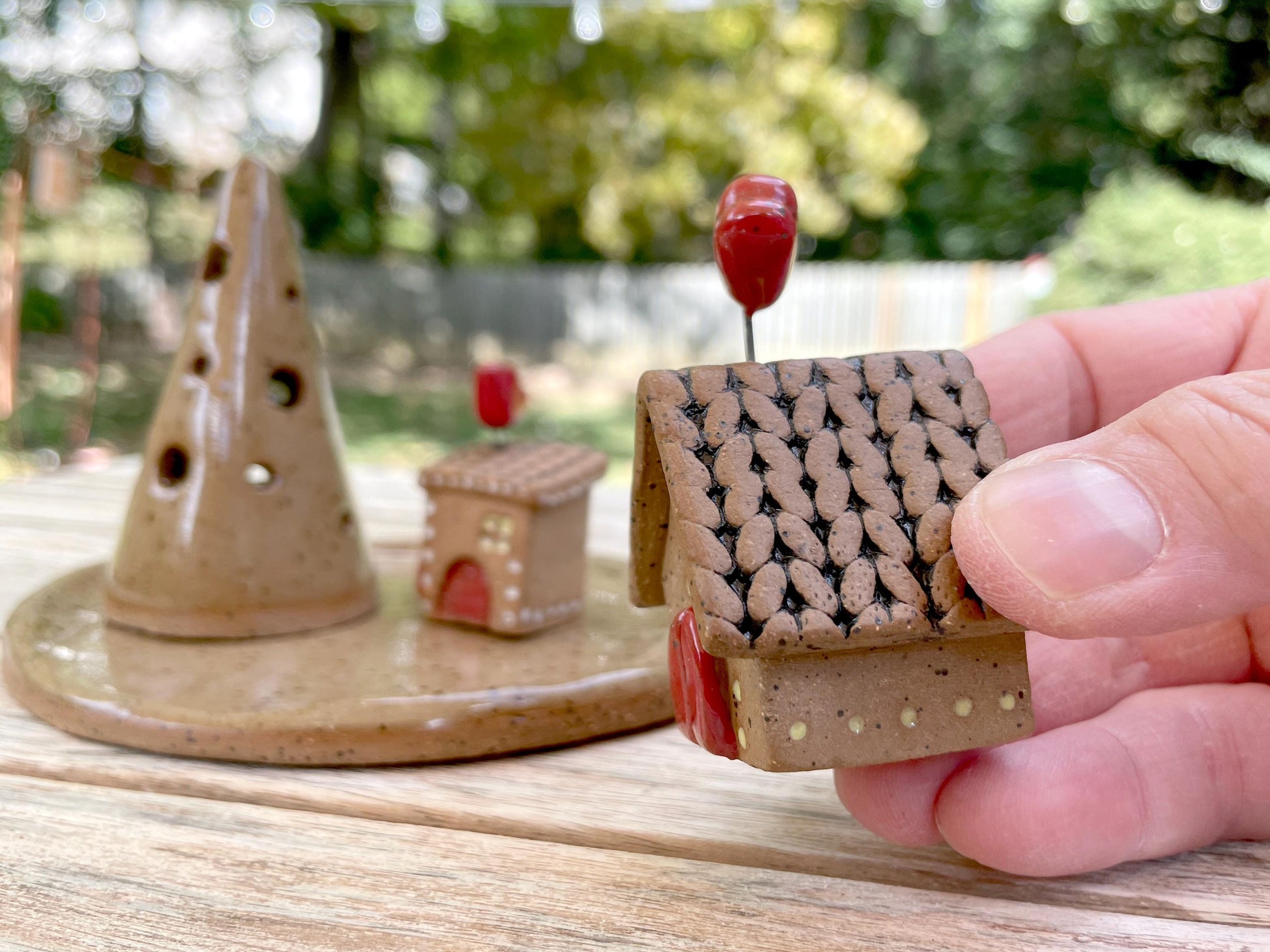 Hand holding a small ceramic house model with a blurred outdoor background
