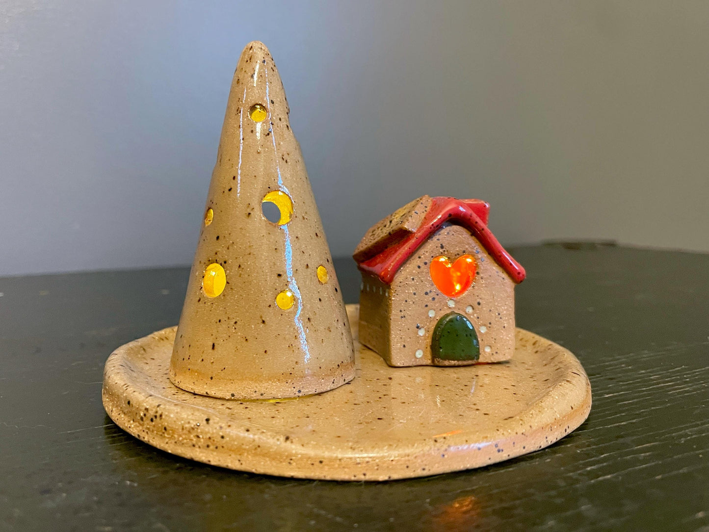 Ceramic Christmas tree and house ornament on a flat surface with a neutral background
