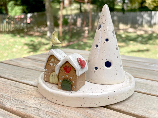 Ceramic gingerbread house and tree on a wooden surface with a garden background